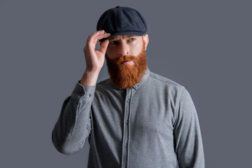 Serious Irish man adjusting cap studio. Portrait of bearded man. Unshaven man with red beard