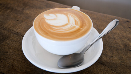 Beautiful golden flat white coffee, white cup and saucer with stainless steel spoon, on a textured...