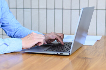 man in blue shirt typing keyboard working on laptop