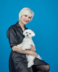 portrait of an adult blonde with a small Maltese lapdog on a blue background