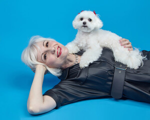 portrait of an adult blonde with a small Maltese lapdog on a blue background