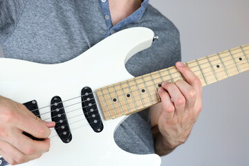 Young man playing chord on white electric guitar