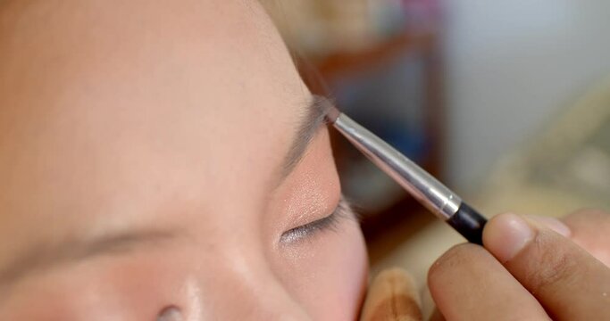 Extream close up, hand holding a brush to detail eyebrows after drawing.