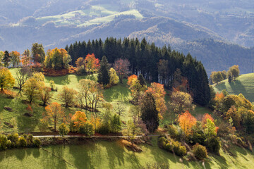 Colorful autumn landscape with mountains at sun shine casting light and shades on hills with  forest in fall colors.