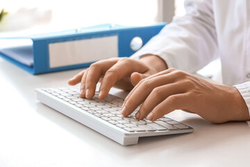 Male doctor working with computer keyboard at table in clinic, closeup