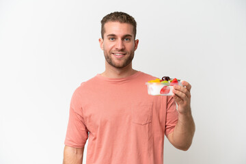 Young caucasian man holding a bowl of fruit isolated on white background smiling a lot