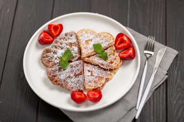 Banana and chocolate waffles with fresh berries and mint leaves, sprinkled with powdered sugar on a plate