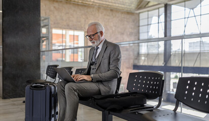Fototapeta na wymiar Senior businessman working on laptop while waiting at subway or railroad train station.