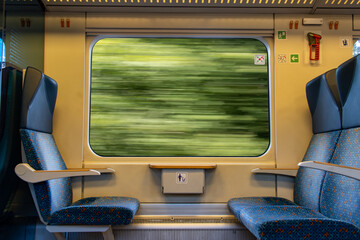 The interior of a passenger train with a view of passing trees outside the window