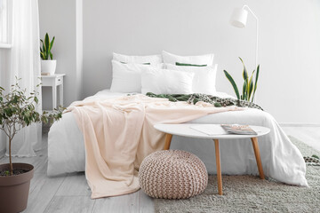 Interior of light room with big bed, houseplants and tables