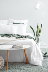 Interior of light room with big bed, houseplant and table