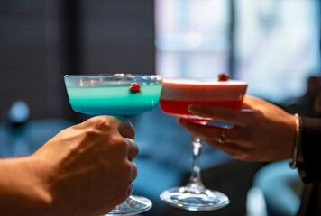 man and woman clinking glasses of alcoholic cocktails in bar
