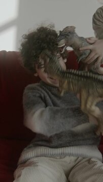 young boys playing with dinosaur toys on red sofa