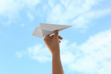 Woman with paper plane against blue sky, closeup