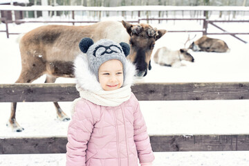 a child near an aviary with a reindeer on a farm in winter