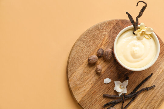 Board with ramekin of tasty pudding, vanilla sticks and nuts on beige background