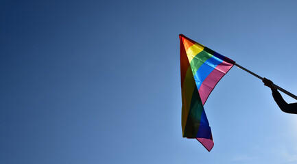 Rainbow flag holding in hand against bluesky background, concept for LGBT celebration in pride month, June, around the world.