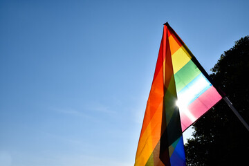 Look up view of rainbow flag, LGBT simbol, against clear bluesky background, soft and  selective focus, concept for LGBT celebration in pride month, June, around the world, copy space.