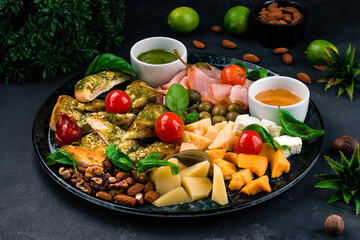 Snacks for wine cheese bread with pesto, pork, assorted cheeses, capers, olives, tomatoes, pesto sauce, walnuts, almonds, basil.