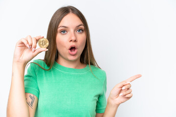 Young beautiful blonde woman holding a Bitcoin isolated on white background surprised and pointing side