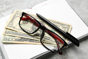 Notebook with eyeglasses, pen and dollar banknotes on grunge background. Budget concept