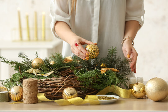 Woman making Christmas wreath with golden balls at table, closeup