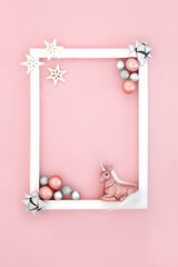 Christmas abstract mythical background on pink with glitter unicorn, snowflakes, round bauble tree decorations and bows with white frame. Festive border design for Xmas and New Year.