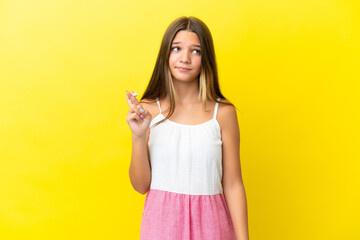 Little caucasian girl isolated on yellow background with fingers crossing and wishing the best