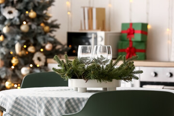 Stand with glasses and Christmas branches on dining table in kitchen