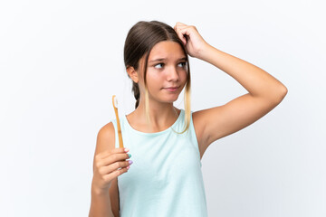 Little caucasian girl holding a toothbrush isolated on white background having doubts and with confuse face expression