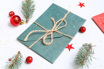 Fototapeta na wymiar Envelope with Christmas decorations and fir branches on light background, closeup