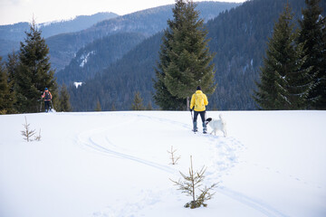 man and dog trekking in big snow in mountains in winter