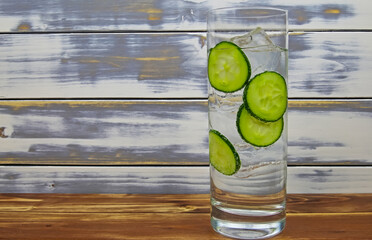 Close up of one isolated cocktail glass with gin tonic cucumber slices and ice cubes. wooden old vintage planks with copy space background.