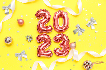 Figure 2023 made of balloons, Christmas decorations and ribbons on yellow background