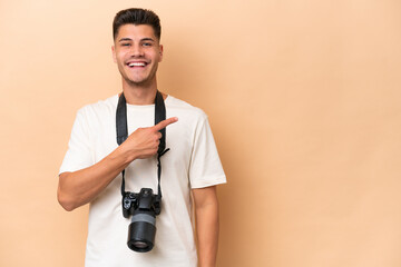 Young photographer caucasian man isolated on beige background pointing to the side to present a product