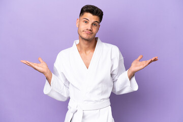 Young caucasian man doing karate isolated on purple background having doubts while raising hands