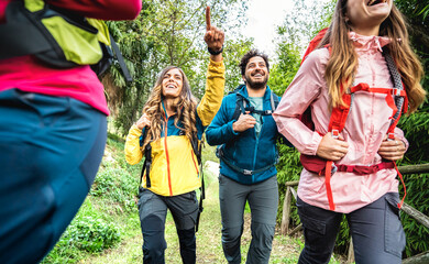 Front view of friends group trekking in forest on italian alps - Hikers with backpacks walking around wild mountain woods - Wanderlust travel concept with young people at excursion - Warm vivid filter