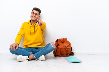 Young student caucasian man sitting one the floor isolated on white background points finger at you with a confident expression