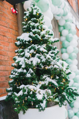 Fototapeta na wymiar Stylish decorated christmas tree outdoor near store window with snow. Winter holidays and decor for xmas