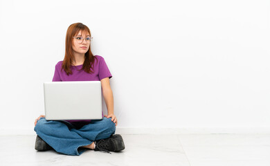 redhead girl with a laptop sitting on the floor looking to the side