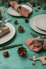 Beautiful table setting with Christmas branches and fir cones on green background, closeup
