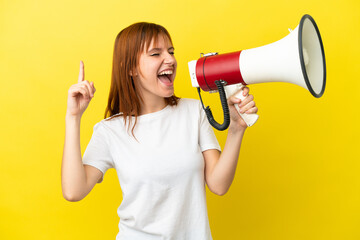 Redhead girl isolated on yellow background shouting through a megaphone to announce something in lateral position