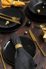 Beautiful table setting with black plates and Christmas balls on wooden background, closeup