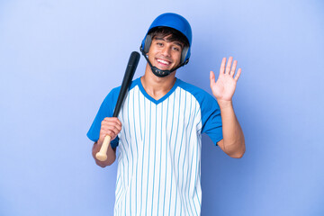 Baseball caucasian man player with helmet and bat isolated on blue background saluting with hand with happy expression