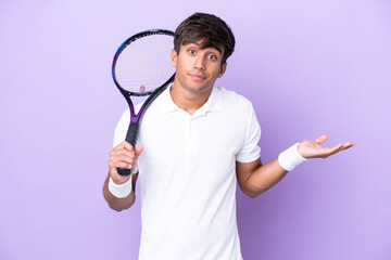Handsome young tennis player man isolated on ocher background having doubts while raising hands