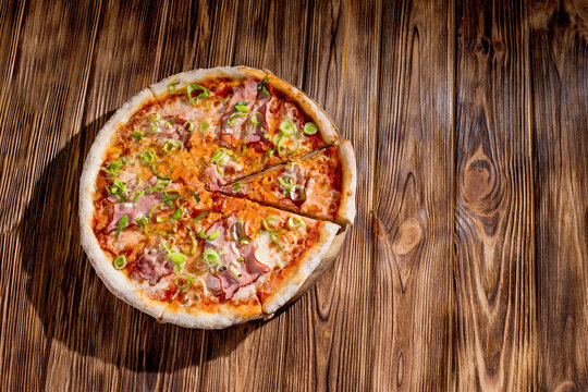 Delicious pizza with mozzarella cheese, ham, leeks on a tomato base on wood background. Copy space
