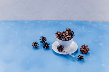 Obraz na płótnie Canvas Dried pine cones on blue background. creative composition with pine cones in white ceramic cup. winter time. diy material for hobbies. copy space