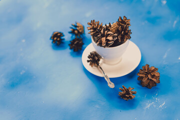 Obraz na płótnie Canvas Dried pine cones on blue background. creative composition with pine cones in white ceramic cup. winter time. diy material for hobbies