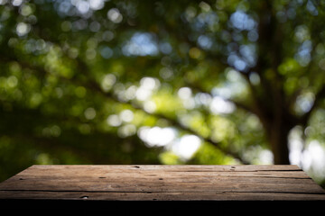 Fototapeta premium Empty wooden board on table top and blur inside abstract green background with natural bokeh, mock up for display of goods.