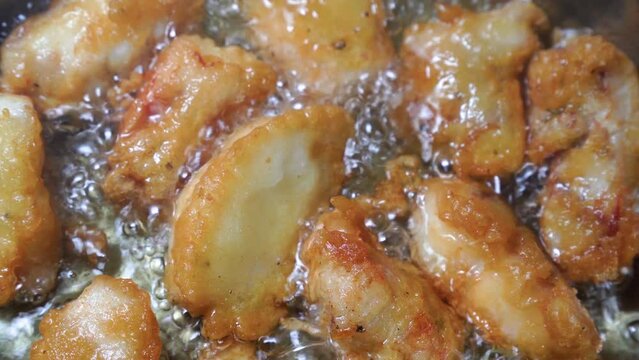 Pieces of fish in batter are fried in boiling oil. Close-up.
